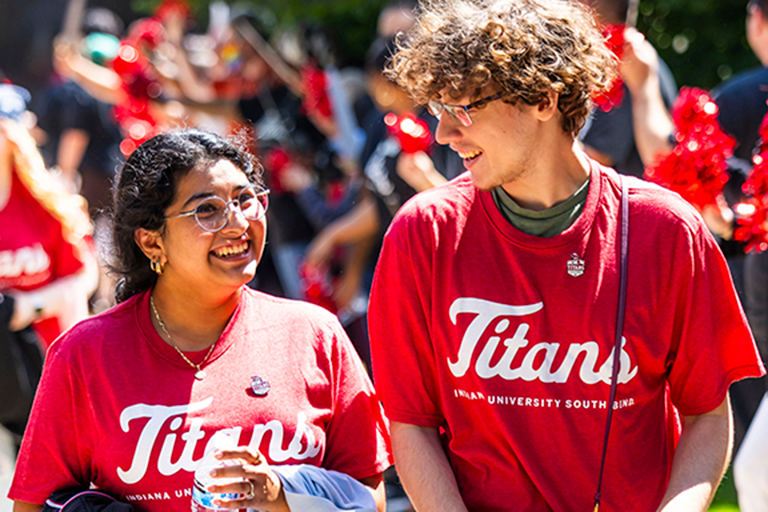 An Asian woman and white man smile at each other while walking outside wearing IUSB Titans shirts